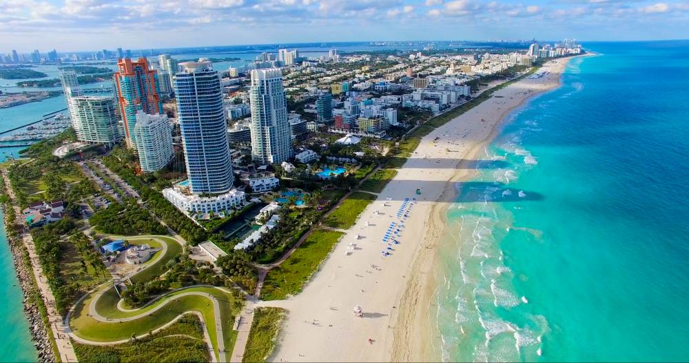 Vista aérea panorâmica de South Pointe Park em Miami Beach, exibindo condomínios de luxo à beira-mar e o cenário vibrante de investimento imobiliário na Flórida em 2025.